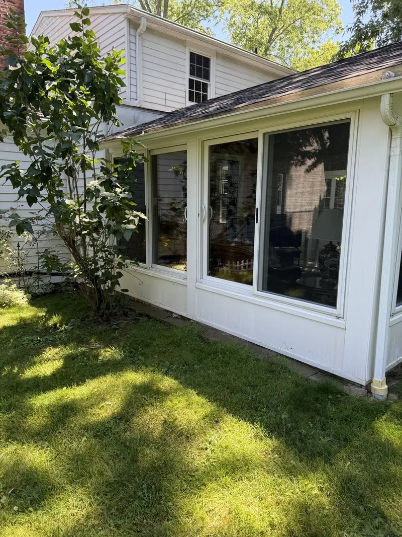 A white sunroom with a wall of windows, seen from the yard
